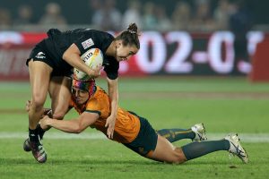 An intense moment in a women's rugby match with one player tackling another to the ground.
