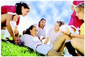 Young female soccer player lying on the grass with teammates and coach gathered around her