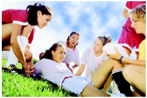 Young female soccer player lying on the grass with teammates and coach gathered around her