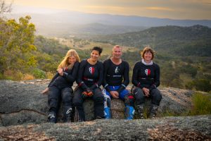 Four happy bikers in protective gear sitting on a rock with a scenic view