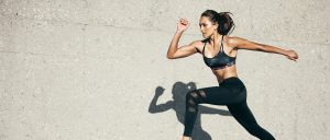 Focused woman running with determination in sports attire on concrete ground
