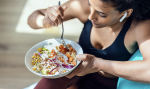 Woman in workout gear eating a healthy, colorful salad after exercise